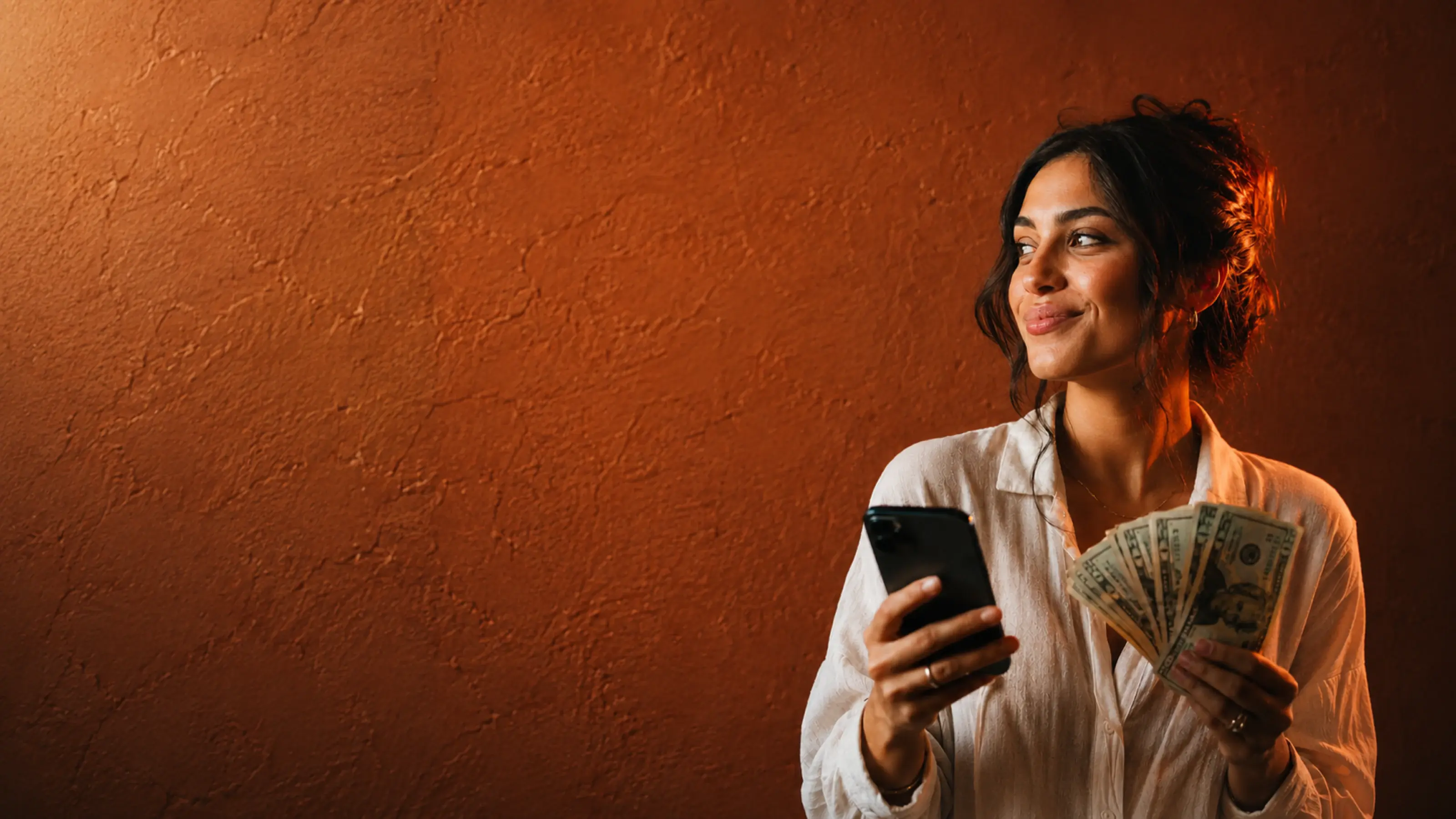 A Hawala customer smiling, holding her phone and US dollar bills earned as cashback.